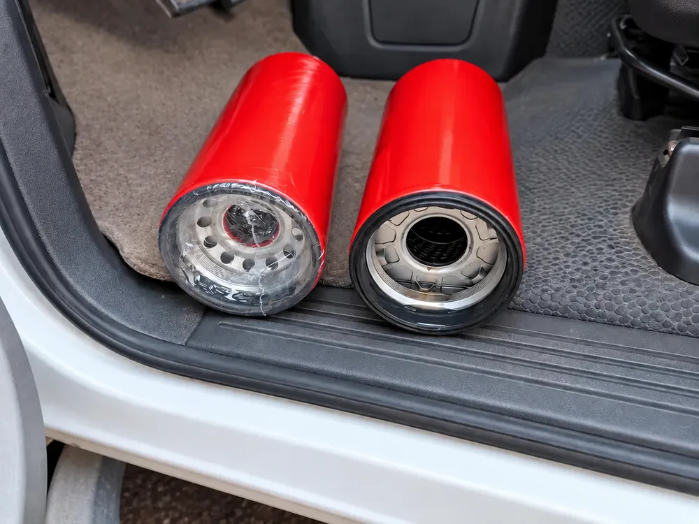 Two Baldwin BT9347-MPG hydraulic filters, one still sealed, on the step of a service truck